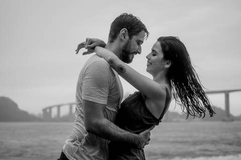 Fotografia preto e branco do casal na chuva. Composição de fundo a terceira ponte de vitória. Capital do Espírito Santo.'
