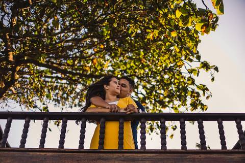 Fotografia no Farol de Santa Lúcia, Vila Velha, ES. Noivo beijando o rosto da noiva. Estão apoiados no beiral do deck.'