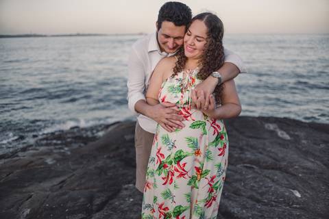 Casal gestante abraçados, sorrindo, com os olhos fechados.'
