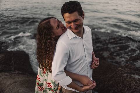 Gestante sorrindo para esposo na pedra da praia. Pousada do Farol e Vila Velha, Morro do Moreno.'