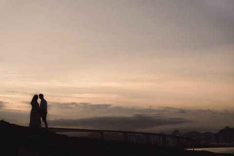 Silhueta do casal em por do sol na pedra da pousada do farol. Vista da terceira ponte de Vitória, ES.'