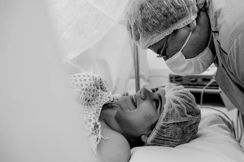 Gestante e marido se olhando na mesa de cirurgia.'