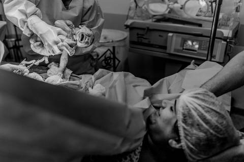 Médico mostrando bebê recém nascido para mamãe.'