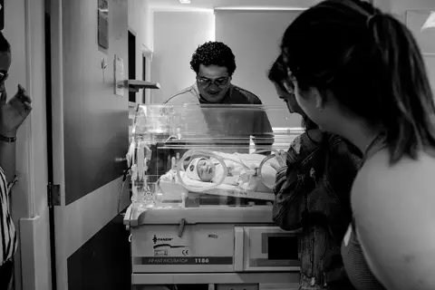 Família contemplando o bebê na sala da maternidade.'
