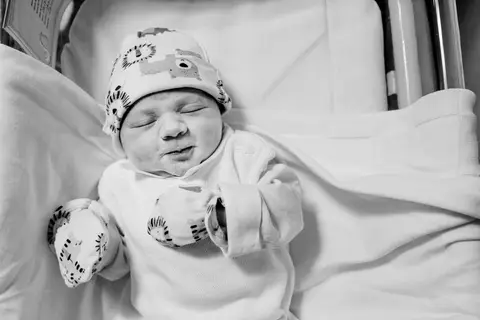 Bebê recém nascido de olhos fechados deitado no berço no quarto do hospital.'