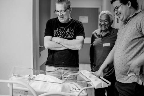 Filho, sogro e pai olhando o bebê no berço.'