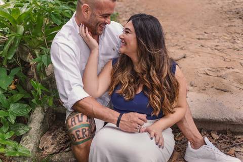 Ensaio Pré Casamento no Jardim Botânico Parque Lage no Rio de Janeiro. Casal sentado na escada de cimento sorrindo um para o outro. Noiva com a mão no queixo do noivo. Abraçados sentado na escada do parque.'