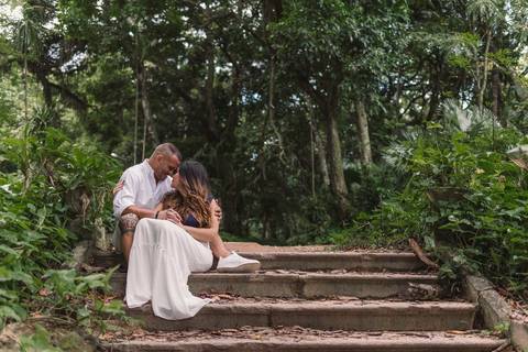 Casal sentando na escada do Parque Lage. Fotografia composta com vegetação do local. Casal está com testas coladas um ao outro.'