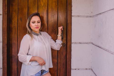 Ensaio fotográfico feminino. Modelo segurando a maçaneta da porta, com seu olhar voltado para baixo e com um leve sorriso no rosto.'