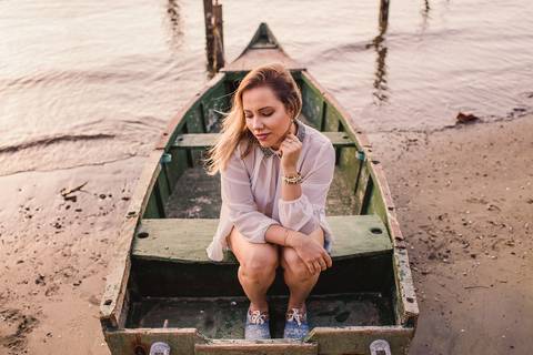 Modelo sentada num pequeno barco de madeira, atracado na Ilha do Frade, Vitória - ES. Ensaio Fotográfico Feminino.'
