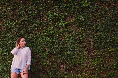 Modelo encostada no muro cheio de plantas trepadeiras.'