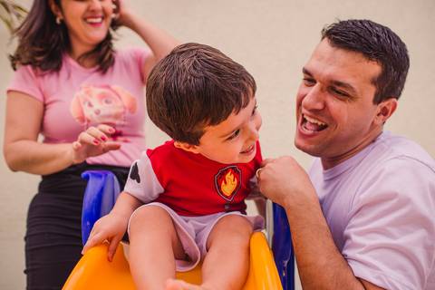 Pais brincando com o filho no escorregador. Documental de Família. Ensaio de família.'