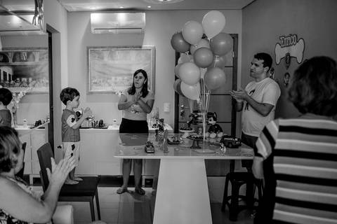 Fotografia preto e branco. Aniversariante na frente da mesa do bolo, cantando parabéns. Fotografia Documental de Família. Itapuã, Vila Velha - ES.'