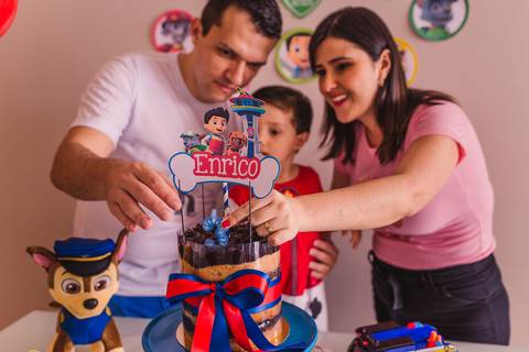 Fotografia da família atrás da mesa de bolo. Preparando para cantar os parabéns para o filho de 3 anos.'