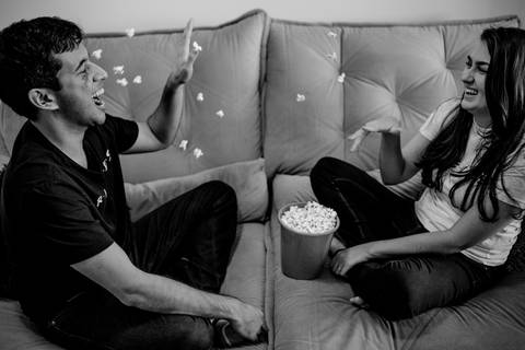 Fotografia preto e branco. Casal jogando pipoca um no outro.'
