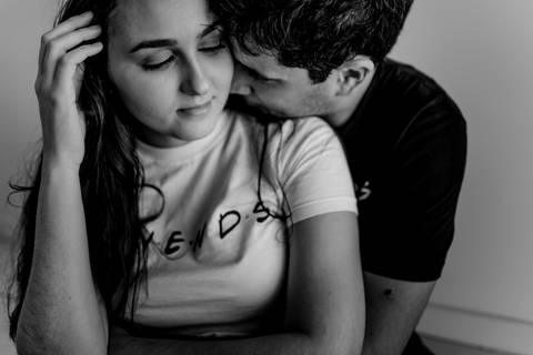 Retrato preto e branco. Casal sentando no chão. Esposo com rosto bem colado ao dela. Aconchegado em sua nuca. Esposa de olhos fechados passando a mão em seu cabelo.
Ensaio fotográfico de casal, realizado em Vitória - Enseada do Suá.'