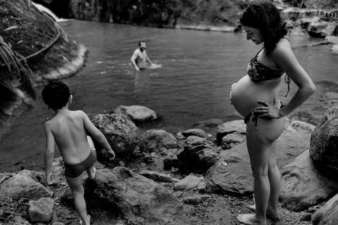 Retrato preto e brando do momento em que filho está entrando na agua. Mãe gravida está observando ele entrar na agua juntamente com o pai. Ensaio fotografico de gestante. Fotografia jornalistica.'