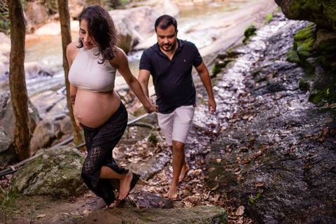 Fotografia do casal no ensaio de gestante de mãos dadas caminhando pelas pedras. ensaio realizado em Viana, na cachoeira.'