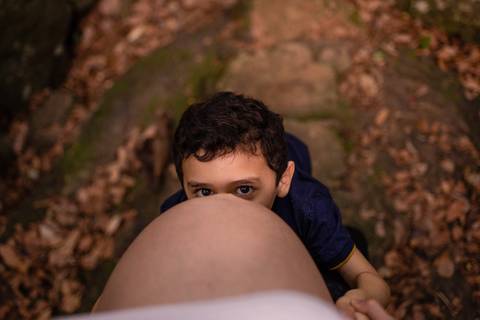 fotografia de ensaio de gestante. filho mais velho se escondendo embaixo da barriga da mãe gravida.'
