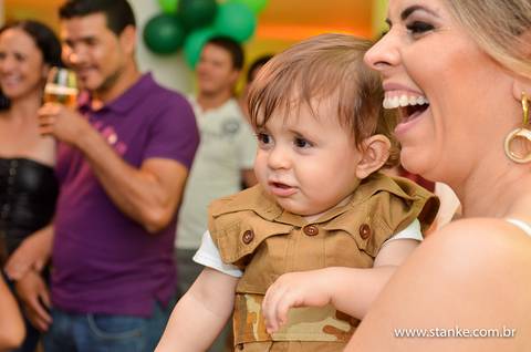 A mãe com super sorriso e com o Lucas no colo, comseus amigos ao fundo no aniversario do Lucas 1 aninho, fotos feita no espaço Parabéns, em Campo Grande-MS.'