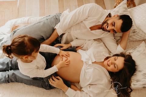 foto grávida e marido brincando com a filha na cama'