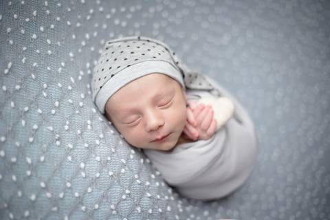 ensaio newborn bebe enroladinho em whap cinza segurando coração'