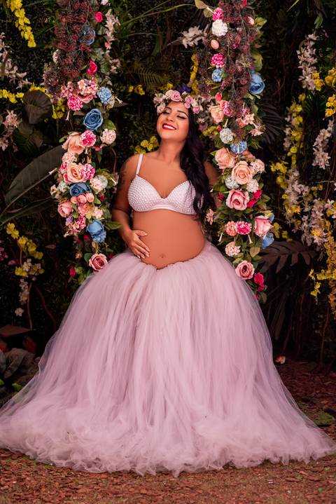 A gestante é retratada em uma pose suave, com as mãos envolvendo delicadamente sua barriga, simbolizando o amor e a proteção materna.'