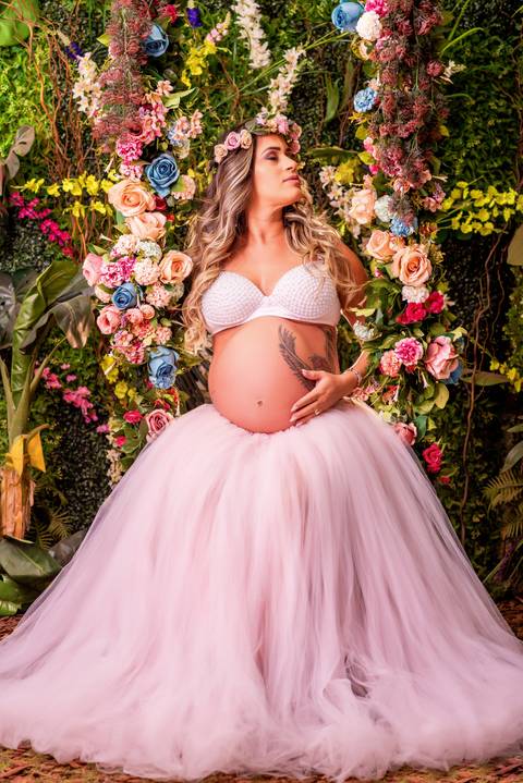 Uma bela gestante sorri radiante no meio do Jardim Encantado, rodeada por flores coloridas e borboletas.'