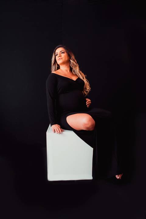 Uma imagem poderosa mostra a futura mamãe destacando sua força e beleza, envolta por um cenário preto que realça sua silhueta.'