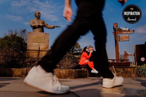 Casal em momento descontraído na Rua Pedro Benetti, Gramado, Rio Grande do Sul, capturado em um contraste dinâmico com a estátua e o movimento dos transeuntes. A fotografia premiada destaca o amor e a energia da cidade.'