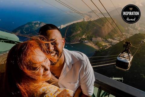 Casal em momento espontâneo e cheio de alegria no Pão de Açúcar, Rio de Janeiro, com vista deslumbrante da cidade ao fundo. Imagem premiada que expressa o amor e a felicidade em um cenário icônico brasileiro.'