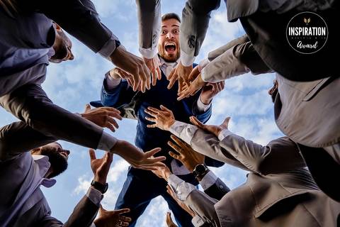 Foto premiada de um noivo sendo erguido no ar pelos padrinhos em um momento de celebração e alegria. Com uma perspectiva única e o céu ao fundo, a imagem transmite a energia e emoção desse dia especial.'