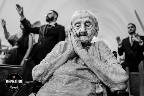 Emocionante retrato em preto e branco de uma senhora em oração durante uma cerimônia de casamento, simbolizando fé, tradição e a profundidade dos sentimentos familiares. A imagem premiada ressalta a importância dos momentos íntimos e espirituais nos casam'