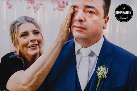 Momento comovente entre mãe e filho no casamento, com a mãe enxugando as lágrimas do noivo. Essa imagem premiada destaca o laço familiar e a profundidade dos sentimentos compartilhados em um dia tão especial.'