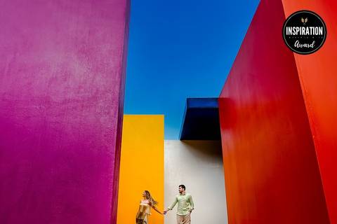 Casal em destaque em meio a blocos de cores vibrantes no Inhotim, Minas Gerais, com céu azul ao fundo. A composição moderna e artística dessa imagem premiada traz uma abordagem única à fotografia de casamento, valorizando a riqueza cultural de Minas.'