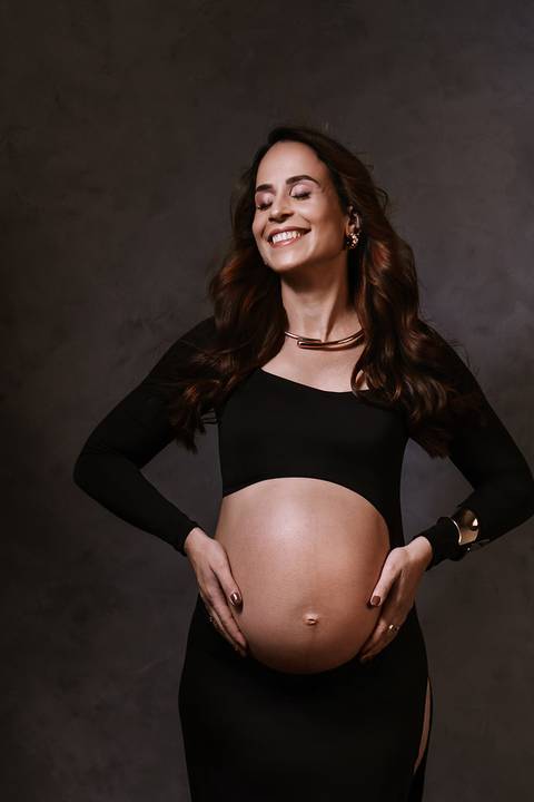 Retrato elegante da gestante com look preto, destacando a beleza da gravidez em um cenário minimalista.'