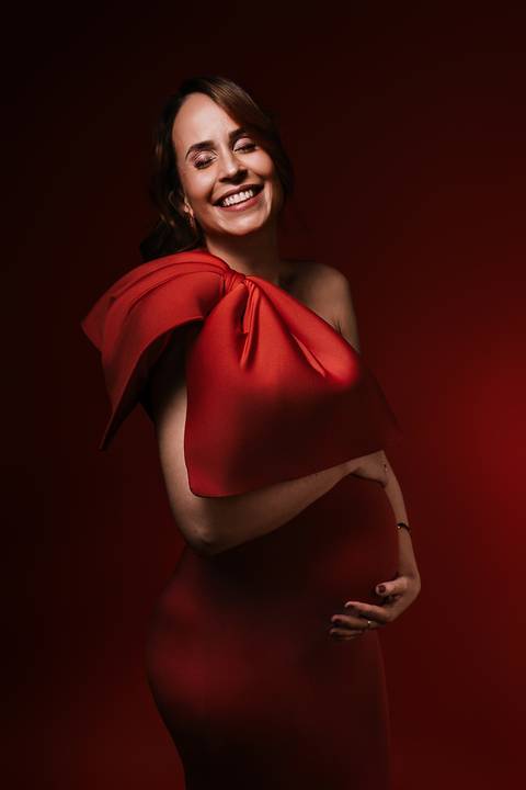 Retrato sofisticado da gestante em vestido vermelho, vivenciando a espera do bebê com elegância.'