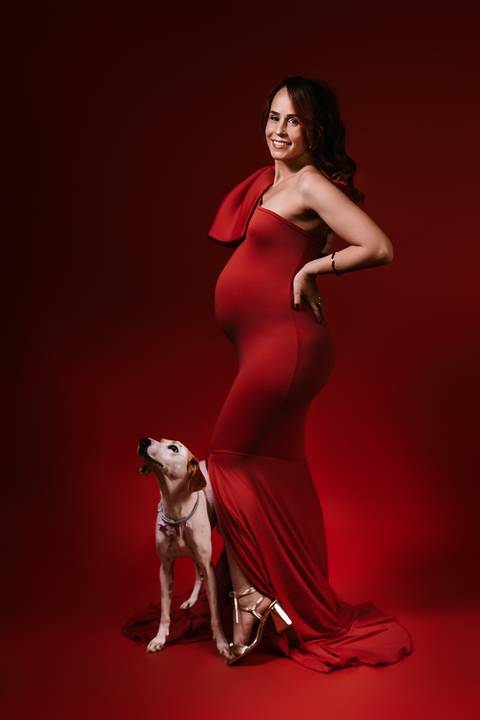 Cena afetiva da gestante em vestido vermelho com a Amora ao lado, marcando a presença da família no ensaio.'