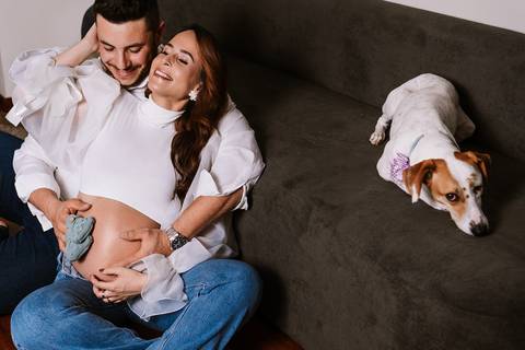 Cena tranquila do casal no sofá com a Amora enquanto celebram a espera pelo Samuel no ensaio de gestante.'