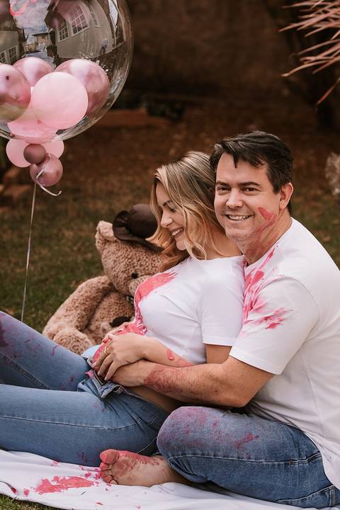 Casal abraçado durante a revelação, com balões ao fundo'