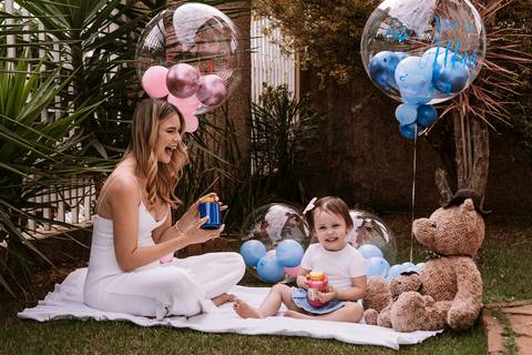 Gestante sentada no piquenique com balões rosa e azul'