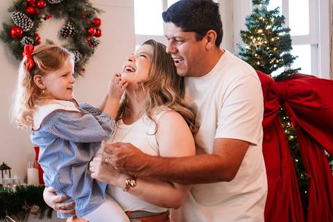 Pais segurando a filha pequena próximo à árvore decorada'