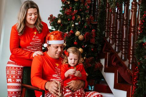 Família abraçada, sorrindo em frente à árvore de Natal'