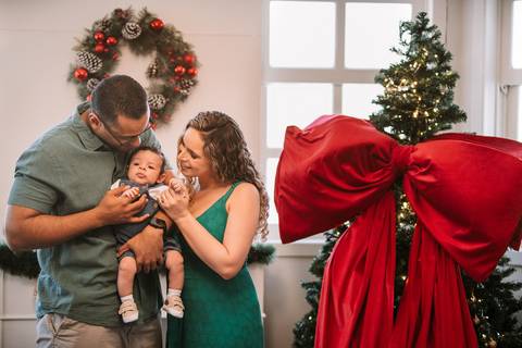 Família reunida diante da decoração de Natal com o bebê no colo'