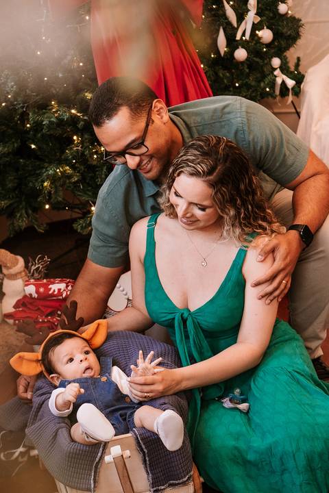 Família sentada no chão montando o cenário natalino com o bebê'
