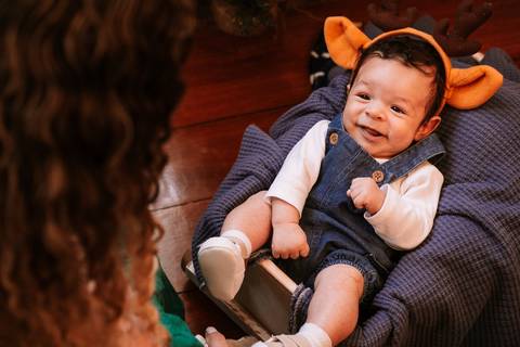  Bebê sorrindo sentado na poltrona com orelhinhas natalinas'