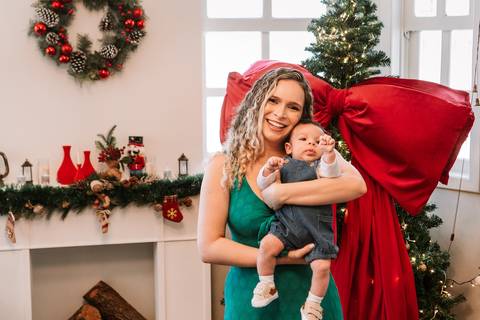 Mãe segurando o bebê diante da guirlanda natalina'