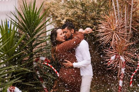 Casal em momento de carinho em área externa decorada para o Natal.'