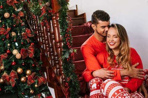 Casal sentado junto à árvore de Natal em clima íntimo.'
