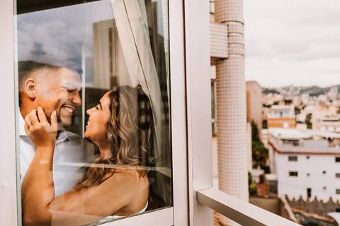 Casal em momento leve na janela do apartamento em Belo Horizonte'